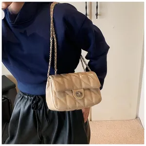 Détail d'un sac bandoulière beige en cuir verni matelassé avec chaîne et fermoir rotatif