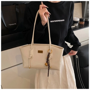 Close-up of beige faux leather tote with decorative knot and golden bell pendant charm