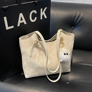 Minimalist beige marble pattern tote bag with plush charm on a black leather sofa