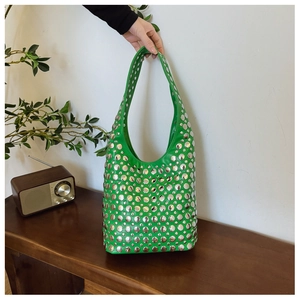 Détail d'un sac cabas vert orné de rivets métalliques argentés sur un banc en bois rétro