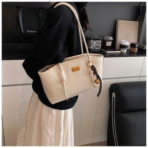 Detail of cream leather shoulder bag with gold hardware and woven rope charm pendant