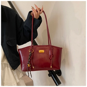 Detail of burgundy glossy underarm bag with gold metal plate and woven pendant