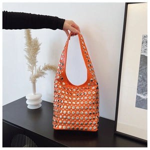Détail du sac seau en cuir orange avec rivets en métal argenté et bandoulière de mode