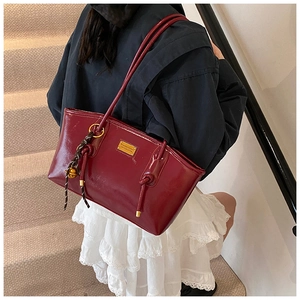 Detail of burgundy leather tote bag with gold logo plaque and woven tassel charm