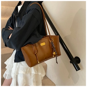 Detail of a brown leather shoulder bag with a gold metal plaque and knot pendant
