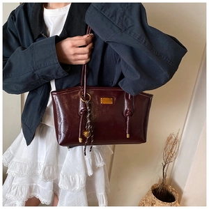 Close-up of dark red patent leather bag featuring gold logo plaque and metallic charms