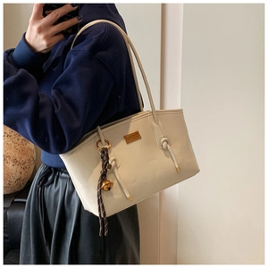 Close-up of cream leather tote bag featuring a gold bell charm and knotted shoulder strap