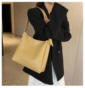 Casual yellow faux leather tote bag with wide strap worn by a model in a modern office