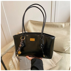 Detail of glossy black shoulder bag featuring a gold fashion plaque and bell tassel