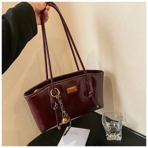 Detail of burgundy patent leather tote bag with gold hardware and tassel charm