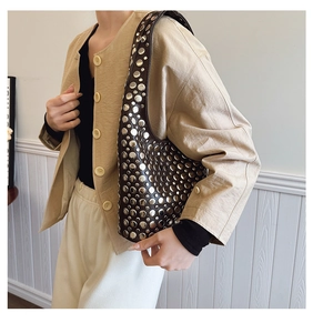 Détail d'un sac bandoulière en cuir foncé orné de rivets argentés au style punk moderne