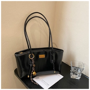 Close-up of black patent leather underarm bag with gold metal logo and side charm