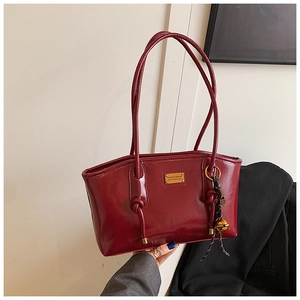 Detail of dark red glossy patent leather tote with gold metal logo and bell charm