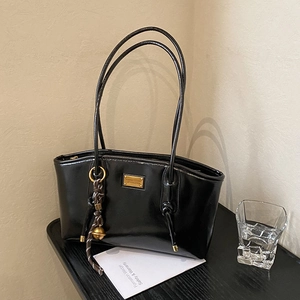 Minimalist black glossy shoulder bag with golden hardware and braided bell pendant detail