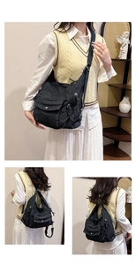 Close-up of black washed denim shoulder bag with multiple functional zippers and pockets