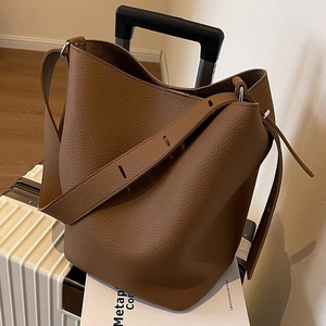 Brown lychee leather bucket bag with wide shoulder strap on a white suitcase