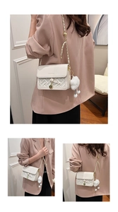 Detail of white woven crossbody bag featuring golden hardware and a plush charm