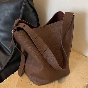 Retro dark brown pebbled leather bucket bag with wide strap on a stone surface