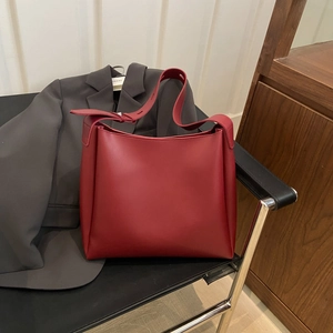 Minimalist large bordeaux red leather tote bag on black chair with grey blazer background