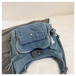 Detail view of denim shoulder bag with multiple zippers and phone inside for scale
