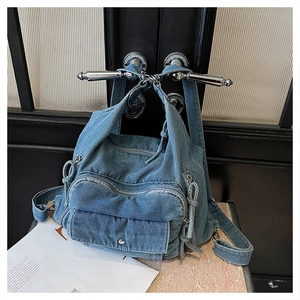 Detail of blue denim backpack with multi-pocket design and adjustable straps on a door