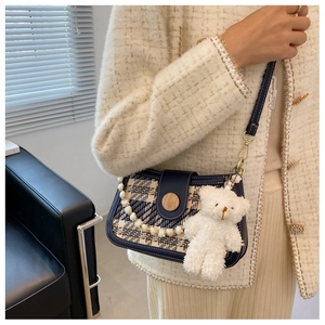 Close-up of a tweed shoulder bag with pearl chain and cute teddy bear pendant