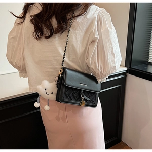 Detail of black woven crossbody bag with gold chain and white cloud plush charm charm