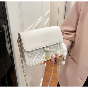 Detail of white chain crossbody bag featuring woven texture and gold charm accessory