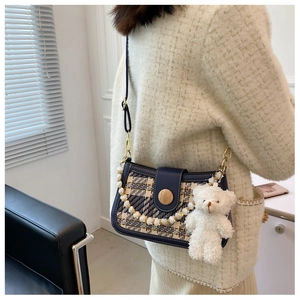 Detail of shoulder bag with beige plaid pattern, shell strap and plush bear pendant