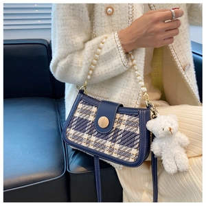 Detail of tweed crossbody bag featuring pearl handle and a plush bear charm on a sofa