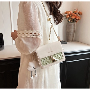 Detail of crossbody bag featuring green woven texture, metal chain and cloud charm