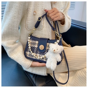 Detail of navy leather bag with plaid fabric, wooden buckle and cute bear pendant