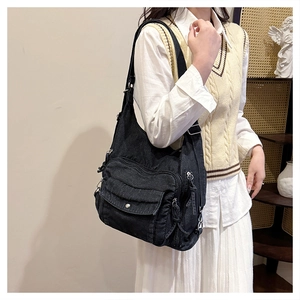Detail of a black washed denim messenger bag with multi-pocket design on a model