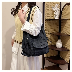 Detailed view of black denim tote bag featuring utility pockets and metallic zippers