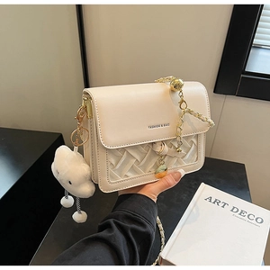 Close-up of cream woven crossbody bag with golden chain and plush cloud charm detail