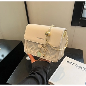 Detail of cream woven crossbody bag with gold chain and green circular pendant