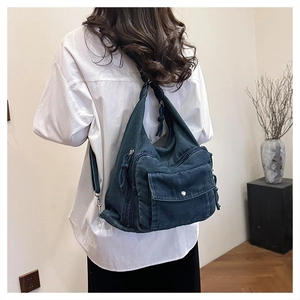 Detail of a dark blue denim crossbody bag with multiple pockets and vintage workwear style