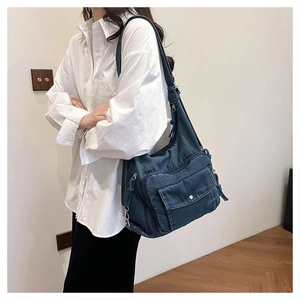 Detail view of a large navy blue denim tote bag with multiple pockets worn by a model