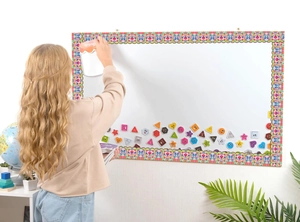Colorful magnetic floral border decoration being applied to a school whiteboard by a girl