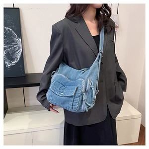 Blue denim crossbody bag featuring multiple zipper pockets shown on a model with a black blazer