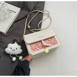 Detail of crossbody bag with pink woven texture, chain strap, and plush cloud charm