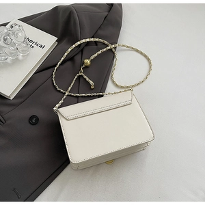 Detail of cream leather crossbody bag with golden chain strap and decorative gold ball charm