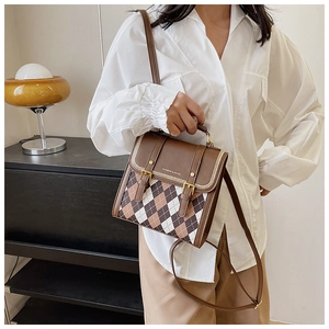 Detailed side view of a brown argyle patterned crossbody bag with gold buckle on display