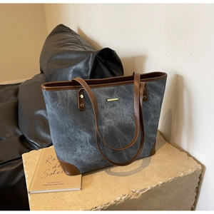 Detail of canvas tote bag with brown leather trim and gold hardware on stone base