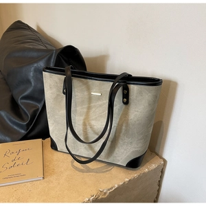 Detail of retro gray suede tote bag with black leather stitching on a stone base