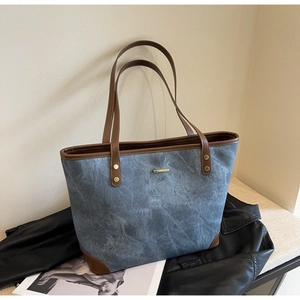 Macro detail of blue denim tote bag featuring brown leather trim and gold metal logo plate