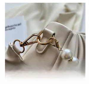 Detail of elegant gold metal hook and large white pearl chain on cream pleated handbag