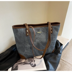 Detail of grey washed denim tote bag with brown leather handles and gold metal trim