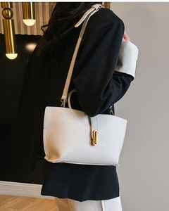 Close-up of white lychee leather texture and golden metal buckle on a shoulder bag