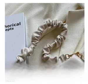 Detail of a creamy beige pleated cloud shoulder strap with elegant gold metal hooks